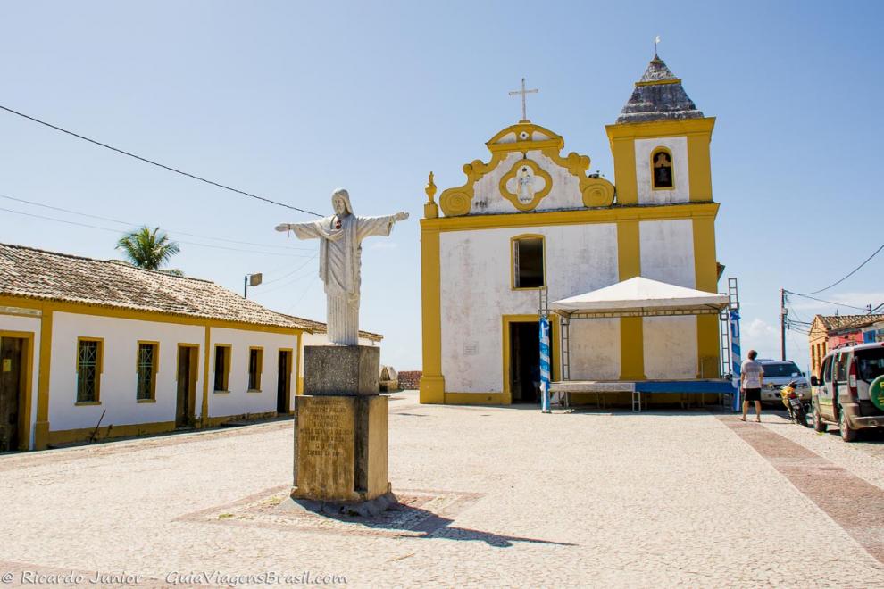 Imagem de Cristo com braços abertos e ao fundo a igreja de Arraial.